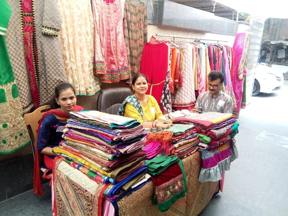Women artisans smiling behind a stall of colourful textiles
